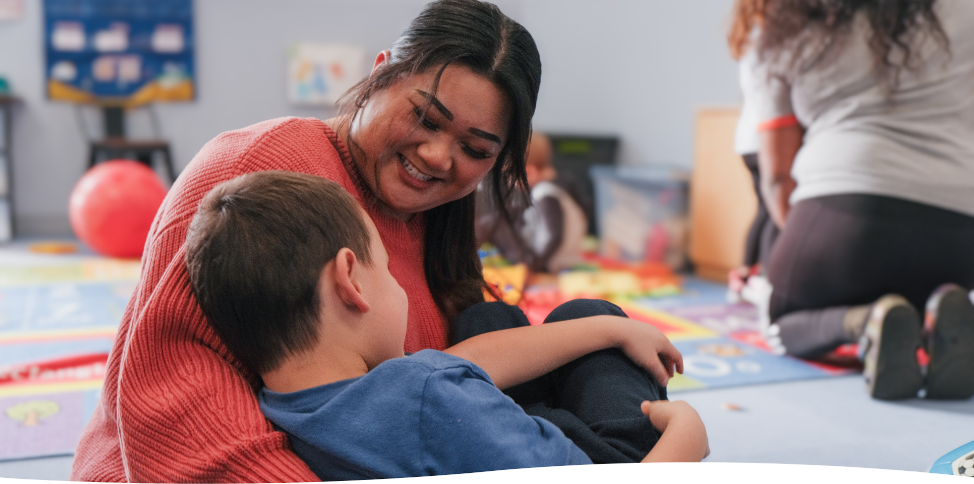 Woman smiling at child in a colorful playroom, creating a warm and friendly atmosphere.