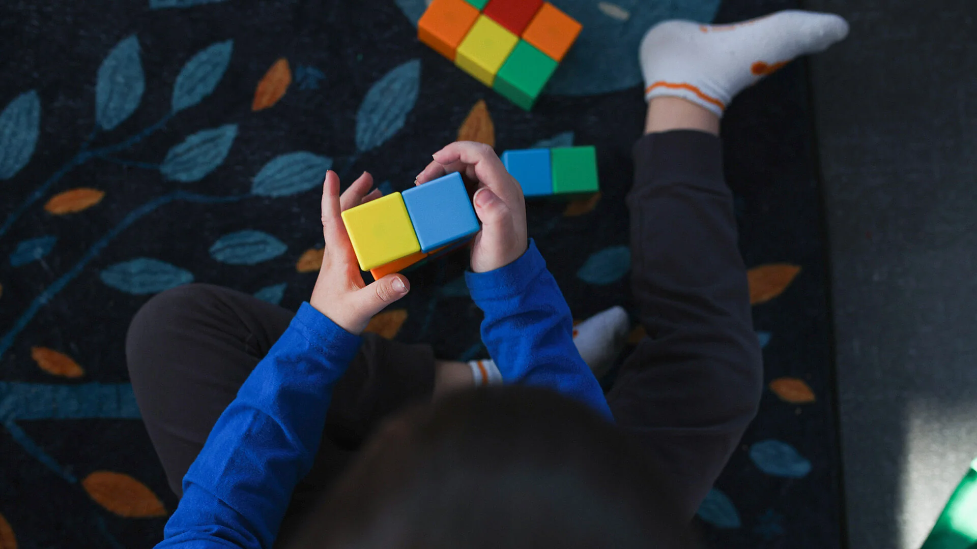 Child playing with colorful blocks on a patterned carpet.