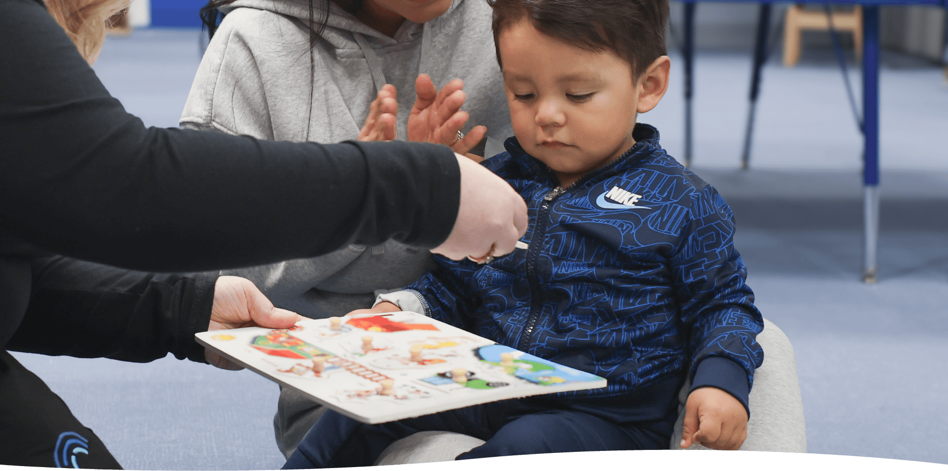 Young child in blue tracksuit engaging with a colorful puzzle board.