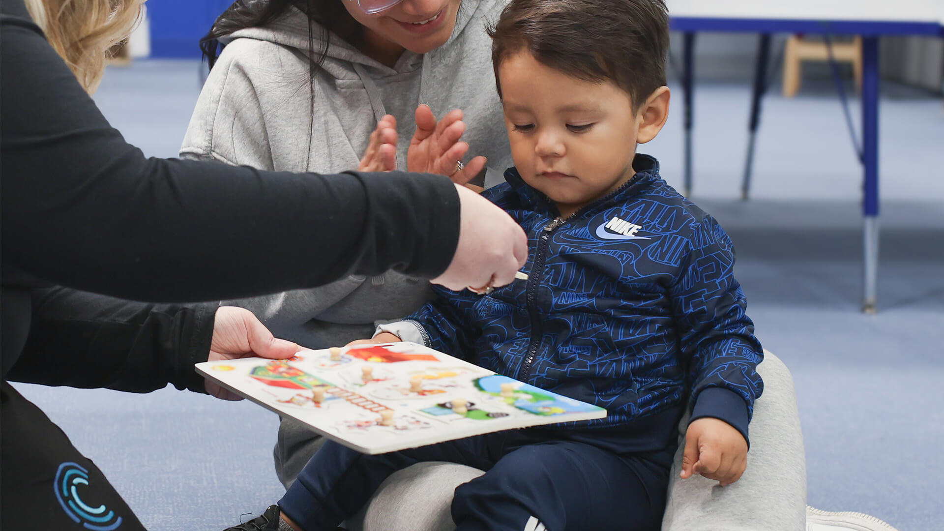 Child playing with a puzzle, assisted by two adults in a learning environment.