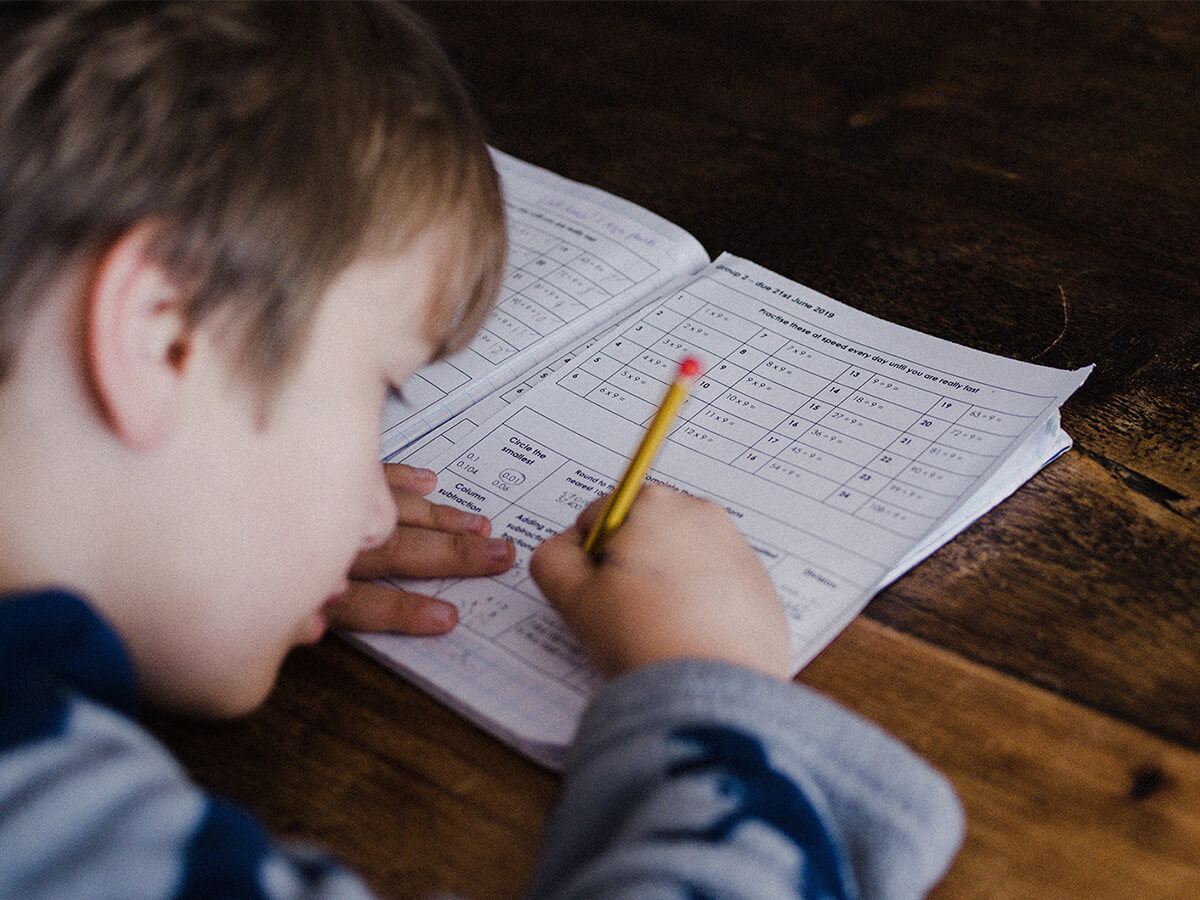 Child focused on solving math problems in a workbook with pencil in hand.