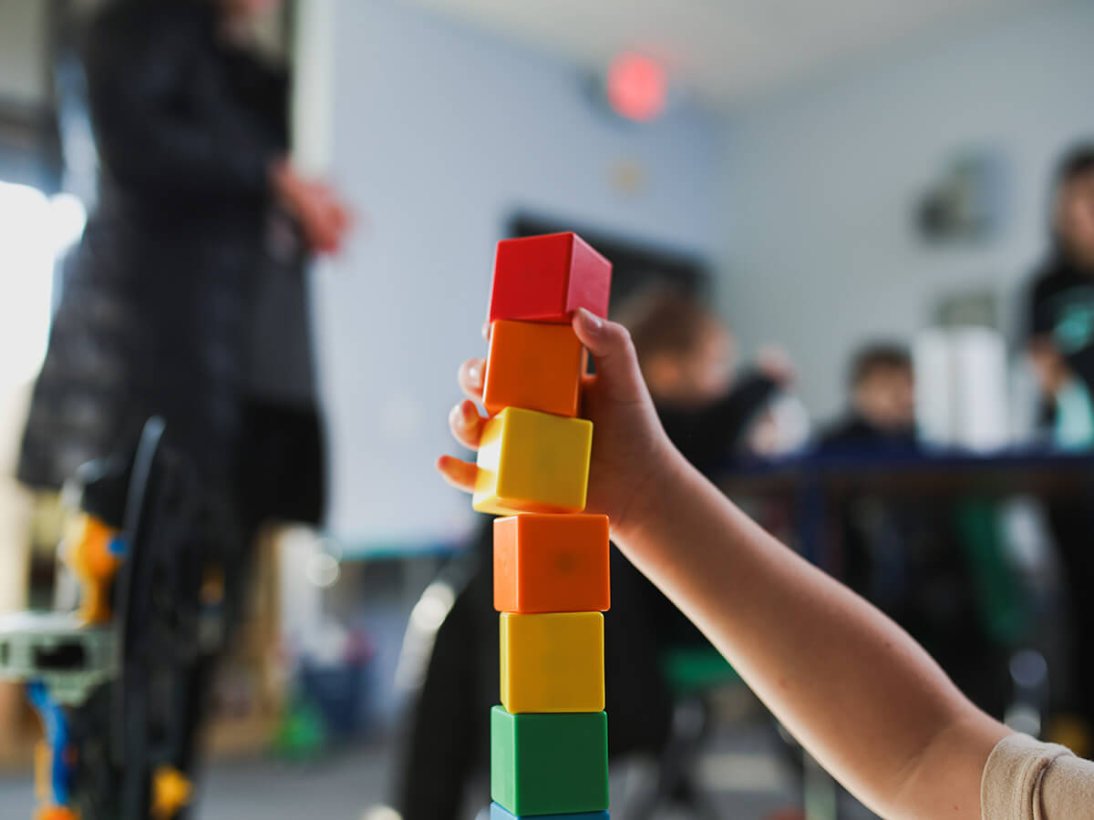 Child stacking colorful blocks in a playroom setting with blurred background.