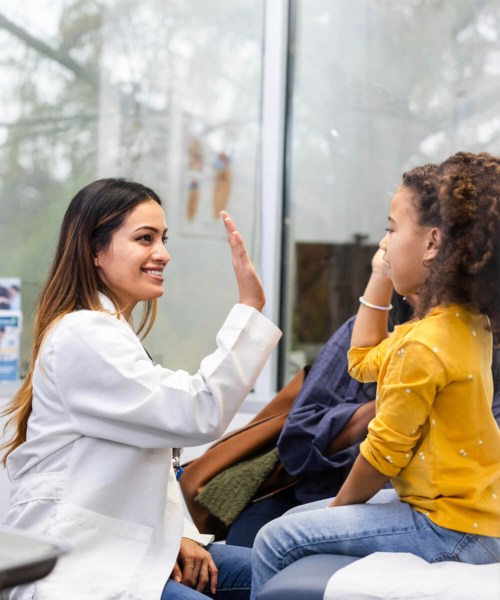 Smiling doctor high-fiving a young girl in a medical office.