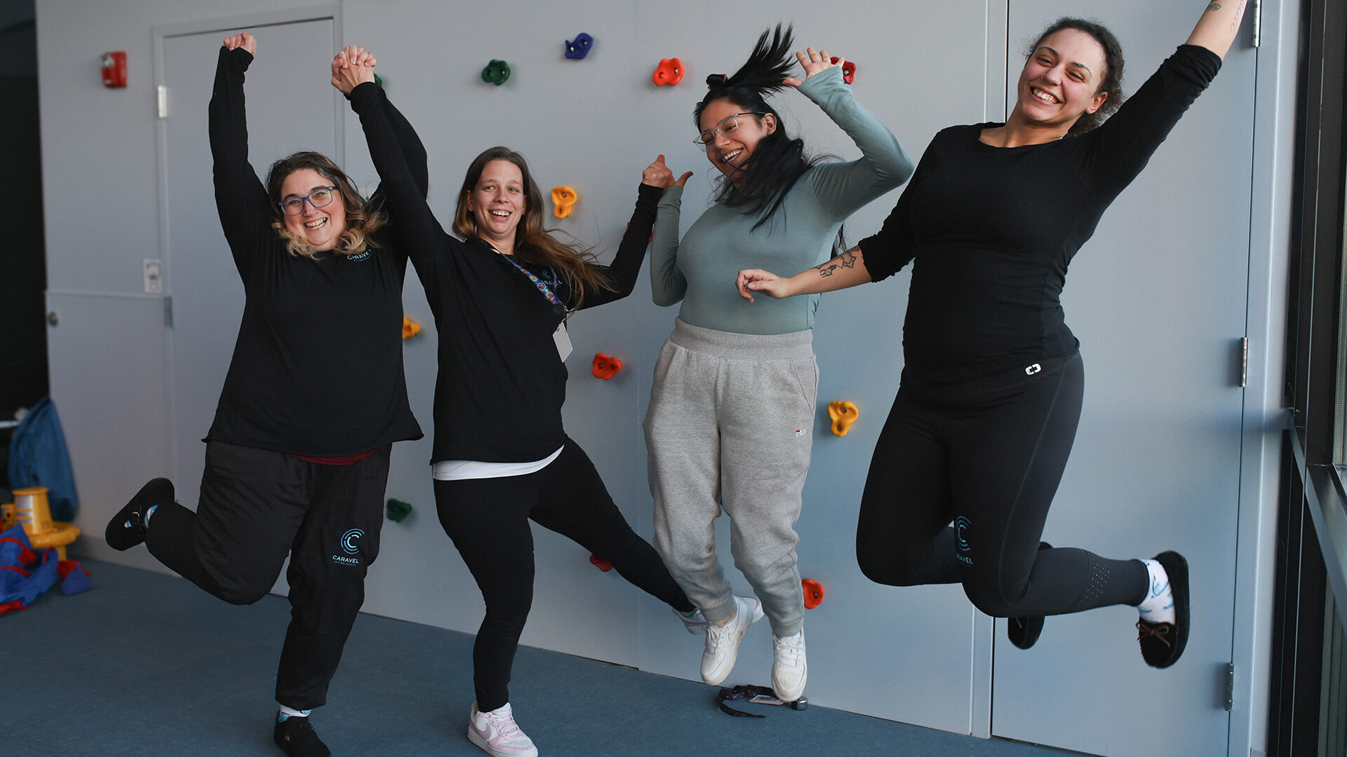 Four joyful staff members jumping in front of a wall with colorful grips.