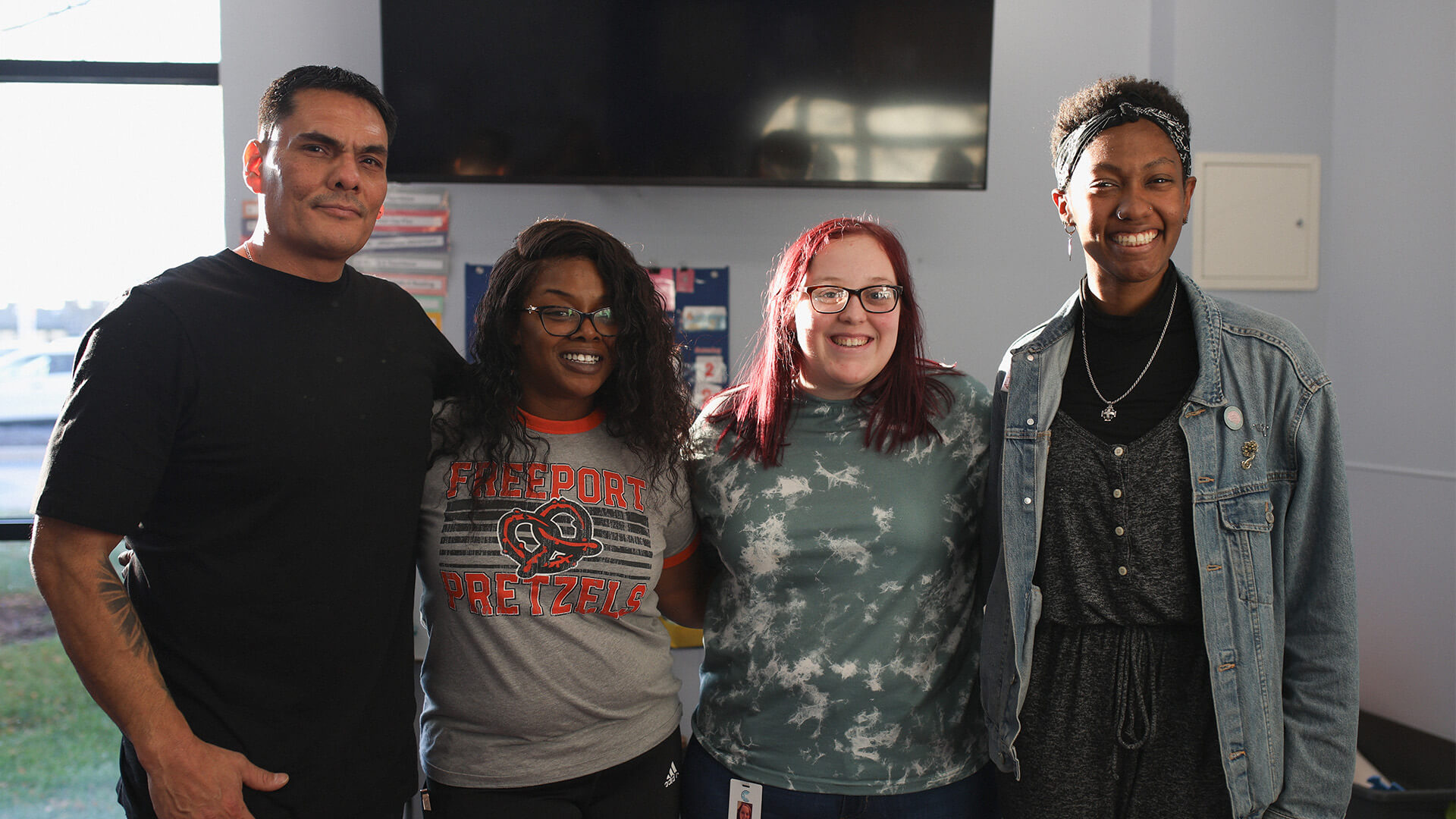 Four smiling people standing together indoors, posing for a group photo.