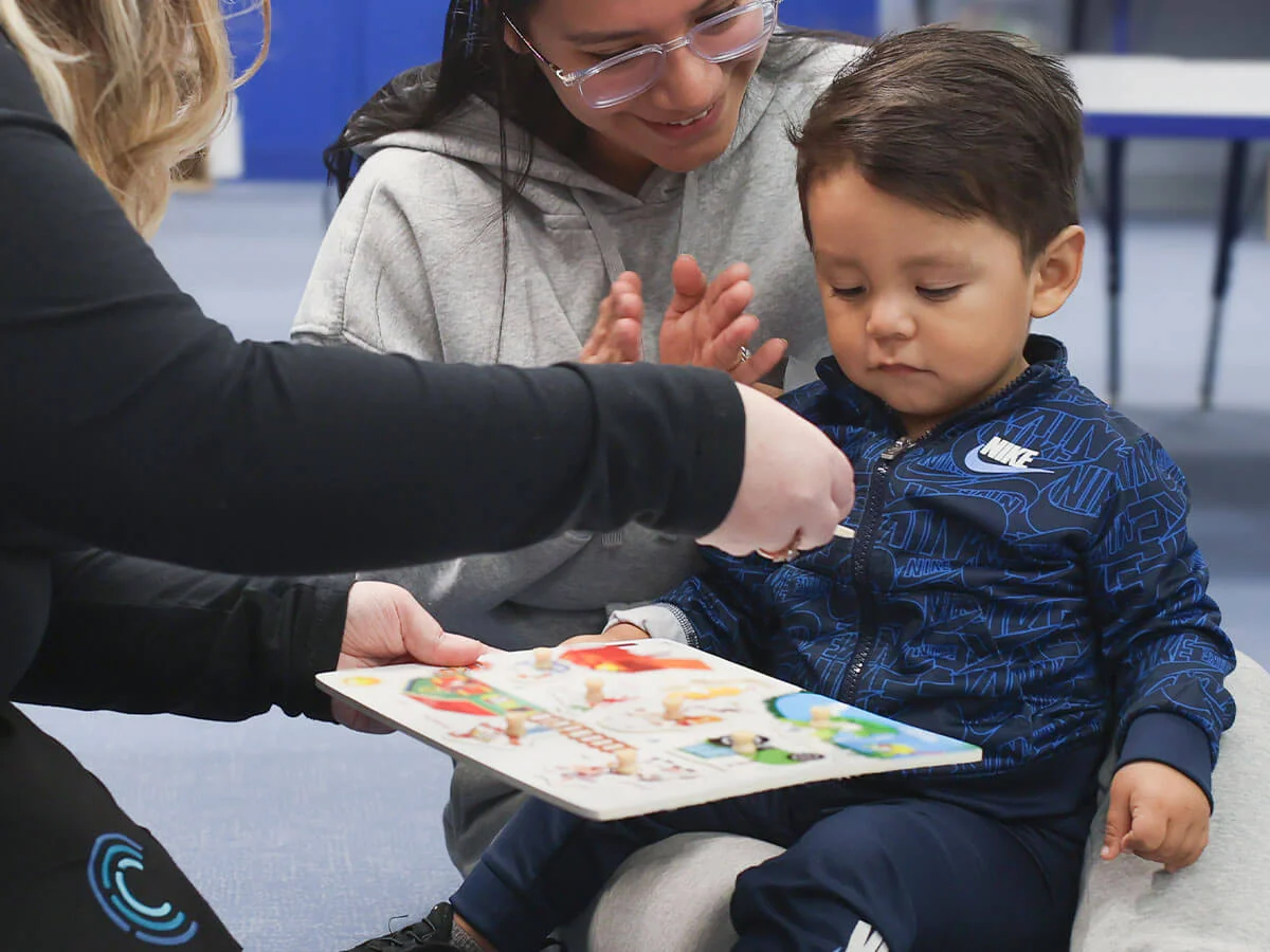 Adult assisting a child with a colorful puzzle while sitting in a room.