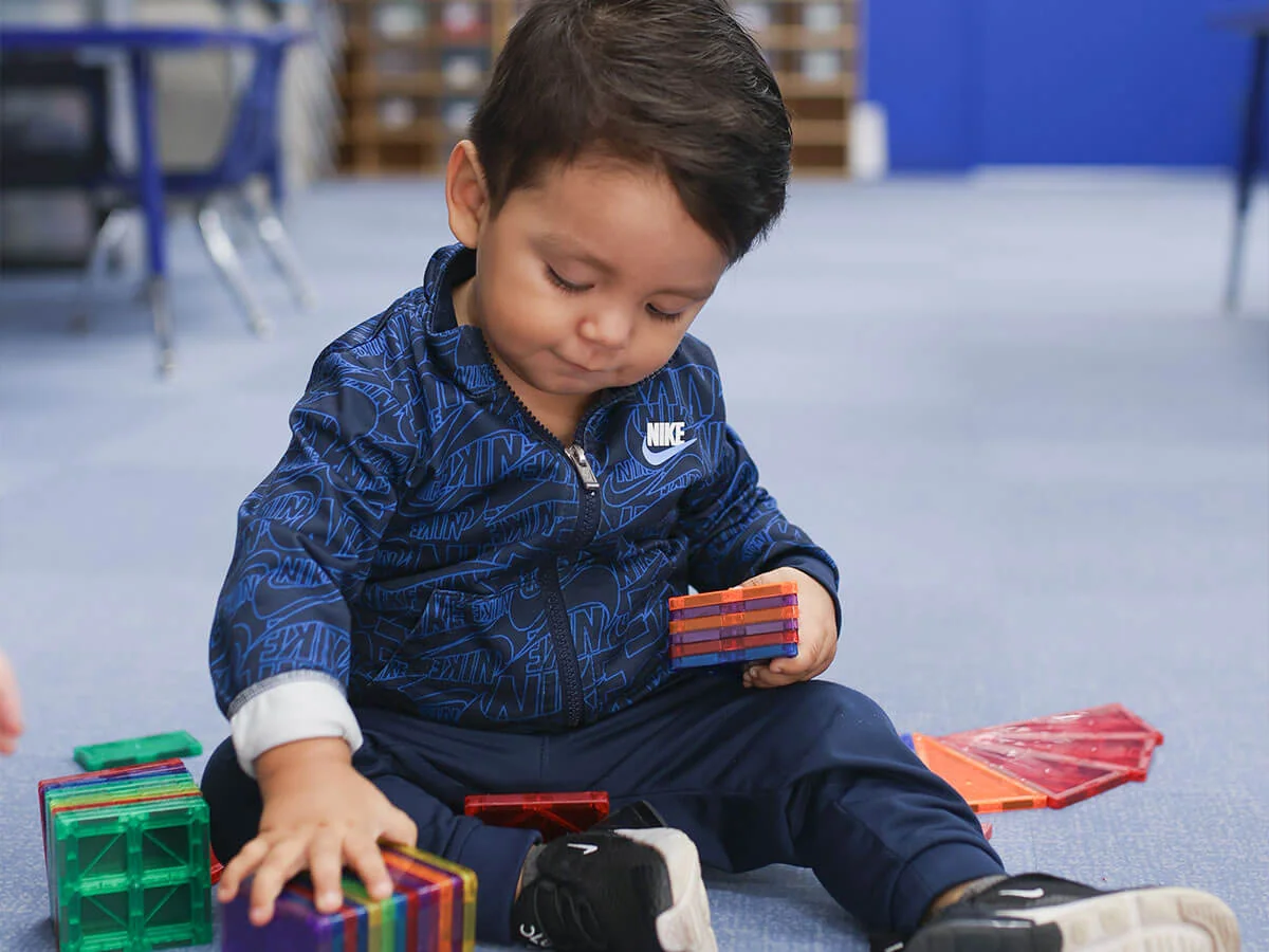 Child engaged in independent play with colorful magnetic tiles indoors.