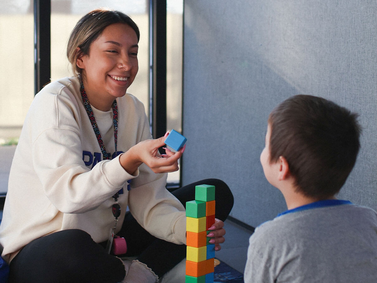 Woman smiling at child as they stack colorful blocks together indoors.