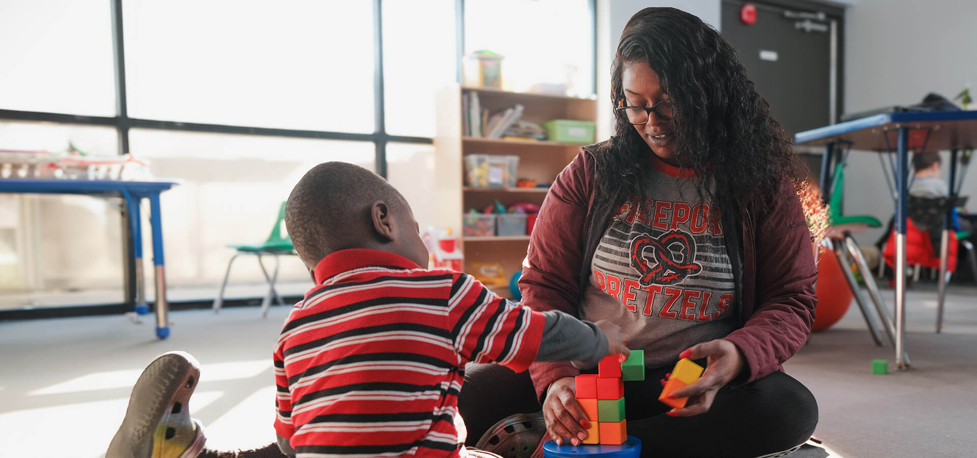 Woman and child building a tower with colorful blocks in a bright room.