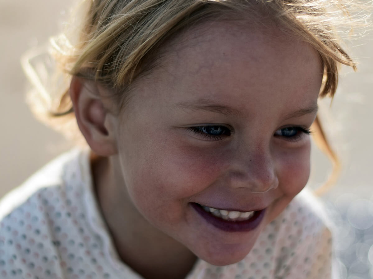 Smiling child with blond hair and a polka dot shirt in soft focus background.