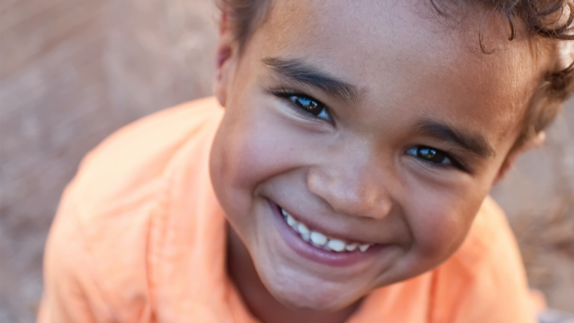 Smiling boy in an orange shirt looking up at the camera with a joyful expression.