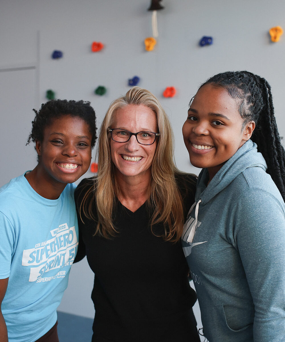 Three smiling people standing together in front of a rock climbing wall.