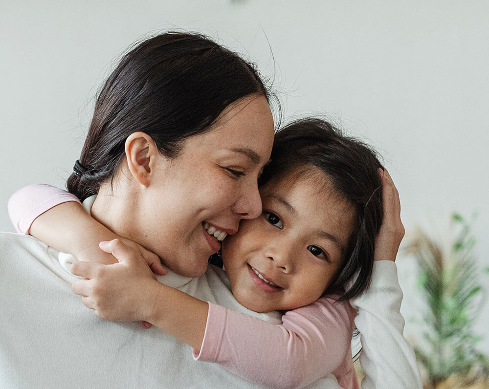 Smiling parent hugging child warmly at home with indoor plants in the background.