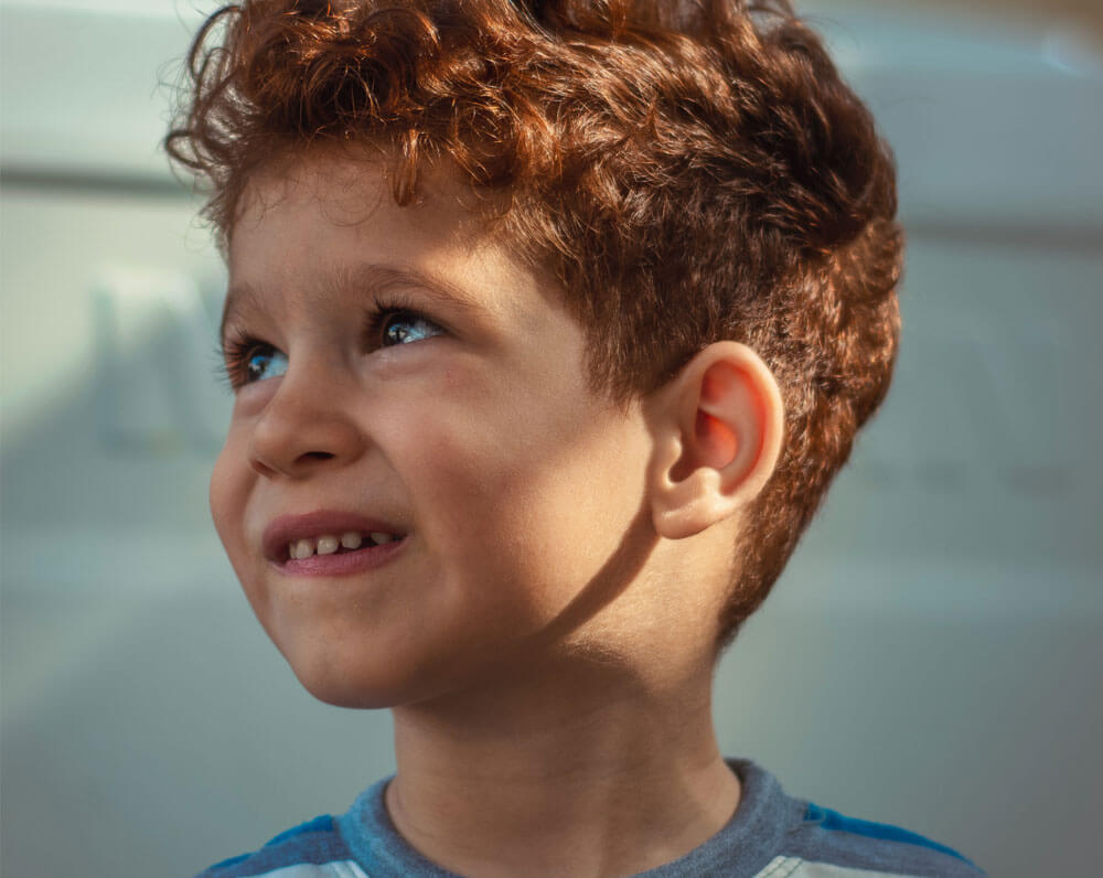 Young boy with curly red hair smiling and looking upwards in soft light.