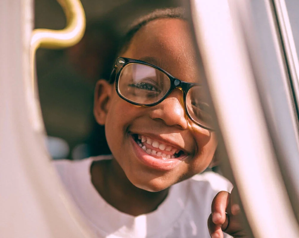 Cheerful child with glasses smiling through a sunny window.
