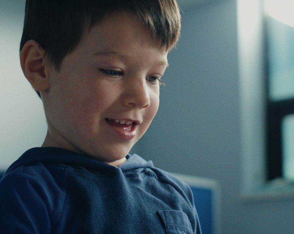 Smiling young boy in blue shirt inside a bright room with soft lighting.