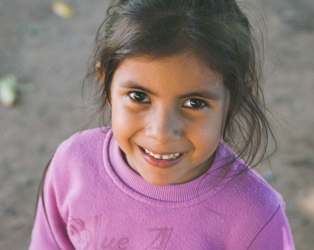 Young girl smiling in a pink sweatshirt, looking up at the camera.