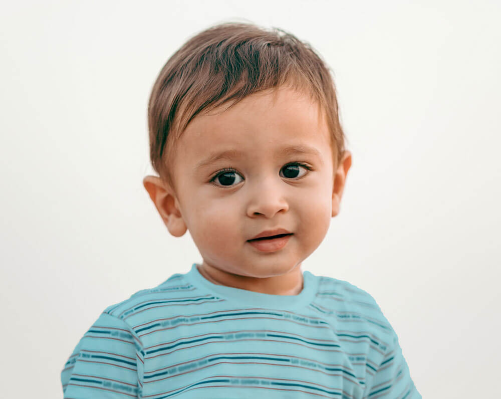 Smiling young boy in a striped blue shirt against a light background.