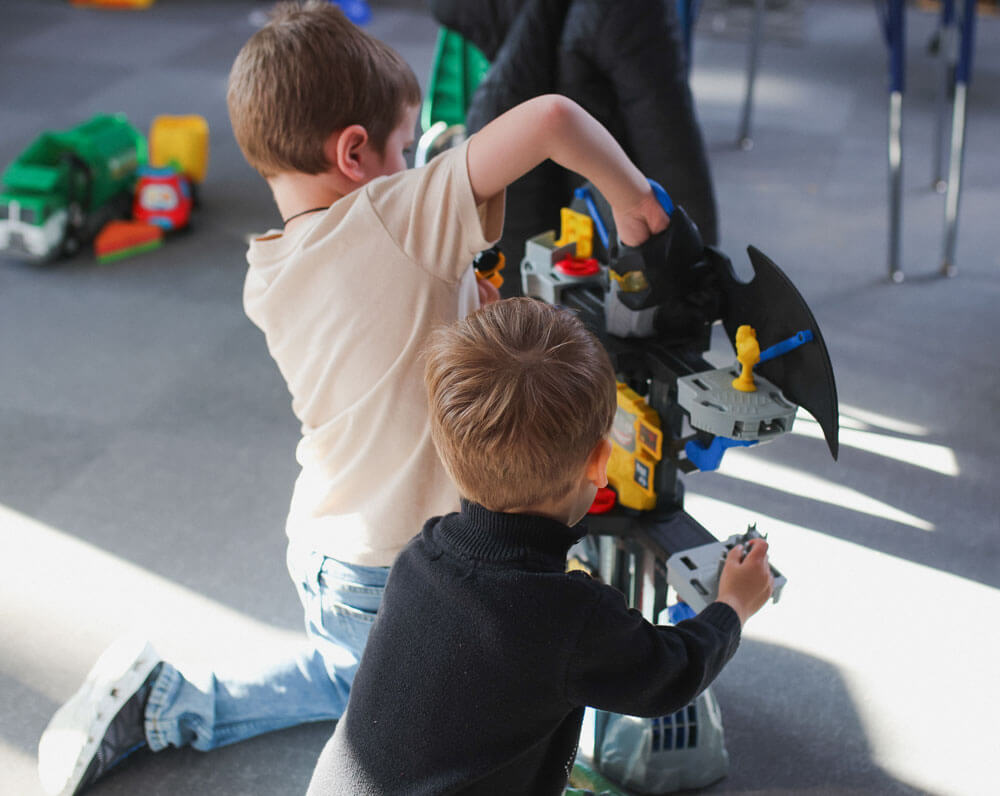 Two young boys playing with action figures in a sunlit room.